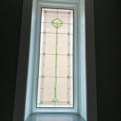 Tall stained glass window with geometric patterns and a central vertical green line ending in a flower shape at the top.