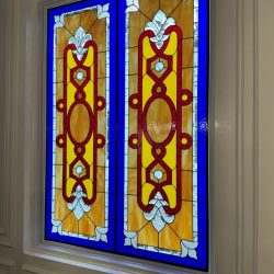 Stained glass window with geometric red, yellow, and blue patterns set in a white wall.