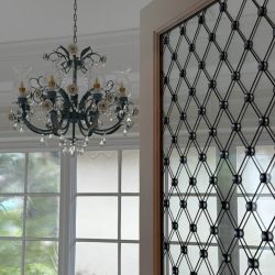 Black chandelier hangs from ceiling near a decorative glass door and large window with greenery outside.