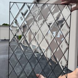 Person holding a rectangular glass panel with a diamond grid pattern in front of a building with a gray wall.