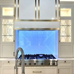 Modern kitchen features a stainless steel stove, blue LED-lit backsplash, white cabinets, and a gooseneck faucet.