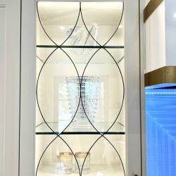 Glass cabinet with geometric design on doors, displaying crystal vase and glass shoes on two shelves.