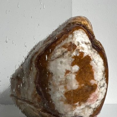 A polished stone is seen through glass, with water droplets on the left half and the right half of the glass dry and clear.