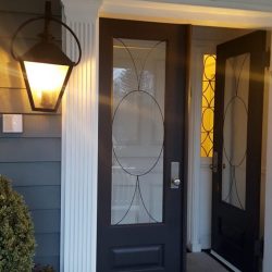 Black front door with glass panels is open, lantern light is on, house number 153 above. Bush and doormat visible.