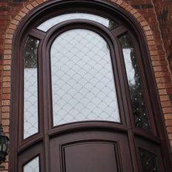 Tall arched wooden door with decorative glass panels set in a brick exterior wall.