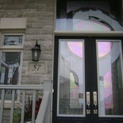 Double door with decorative stained glass, house number 57, stone exterior, window, lantern, and railing visible.