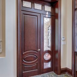 Dark wood door with decorative glass panels stands on a polished stone floor next to a wall thermostat and light switches.
