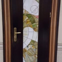 Dark wooden door with a vertical stained glass panel featuring abstract green, yellow, and white patterns.