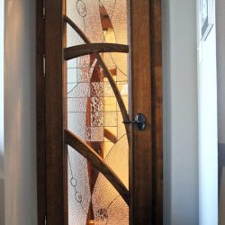 Wooden door with an abstract-patterned glass panel, showing a glimpse of a brightly lit room behind it.