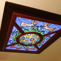 Stained glass ceiling panel with an angel design, blue background, and floral patterns bordered by dark wood trim.