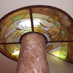 Stained glass ceiling with abstract patterns supported by a polished marble column.