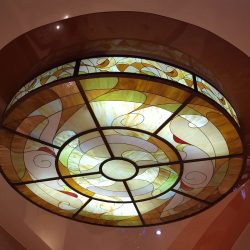 Circular stained glass ceiling light with geometric and swirl patterns in yellow, white, and brown tones.