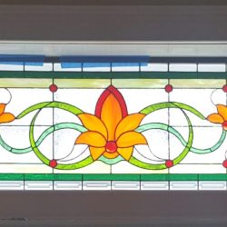 Rectangular stained glass window with orange and yellow floral design, green loops, and red accents.