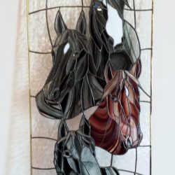 Stained glass artwork of four colored horse heads on textured clear glass, framed in gold.