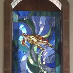 Stained glass window depicting a sea turtle swimming among blue and green water-like patterns with bubbles.
