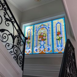 Stained glass window with floral designs seen from a staircase with decorative black railings.