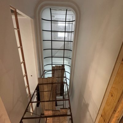 Scaffolding set up under a large, arched skylight in a white-walled room under construction.