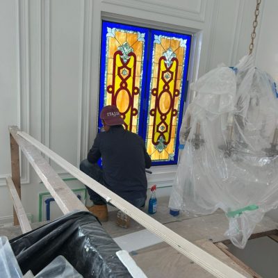 Person in a red cap cleans a vibrant stained glass window in a room under renovation.