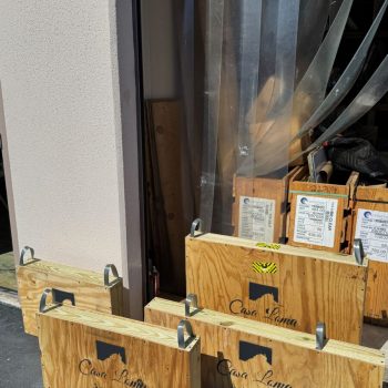 Wooden crates labeled “Casa Loma Art Glass” are stacked by a doorway with clear plastic curtains.